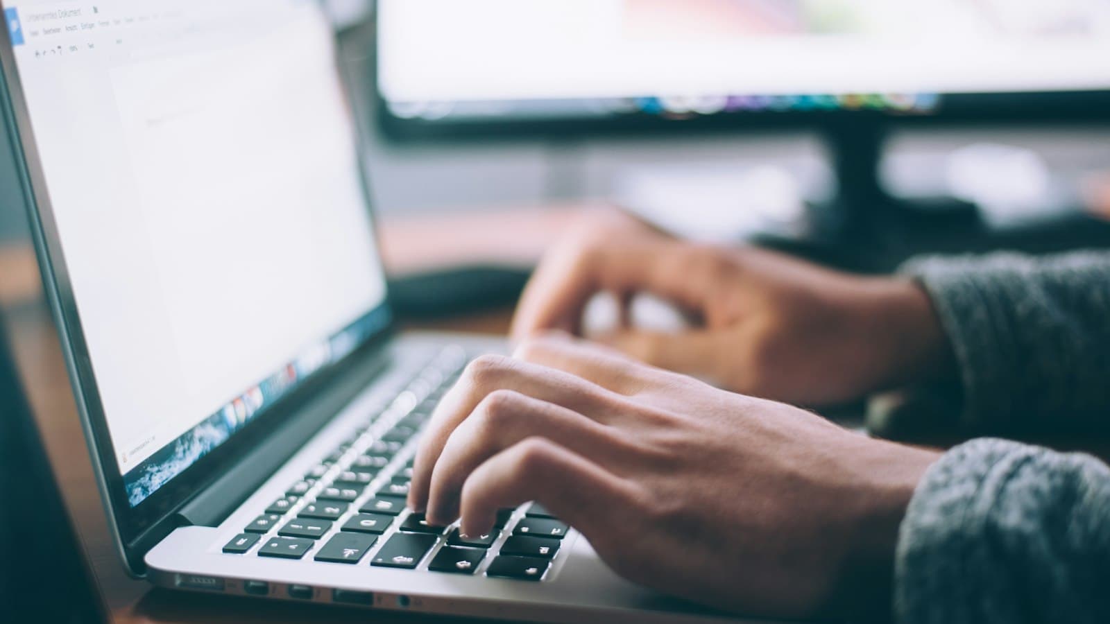 Person typing on a laptop at a wooden desk